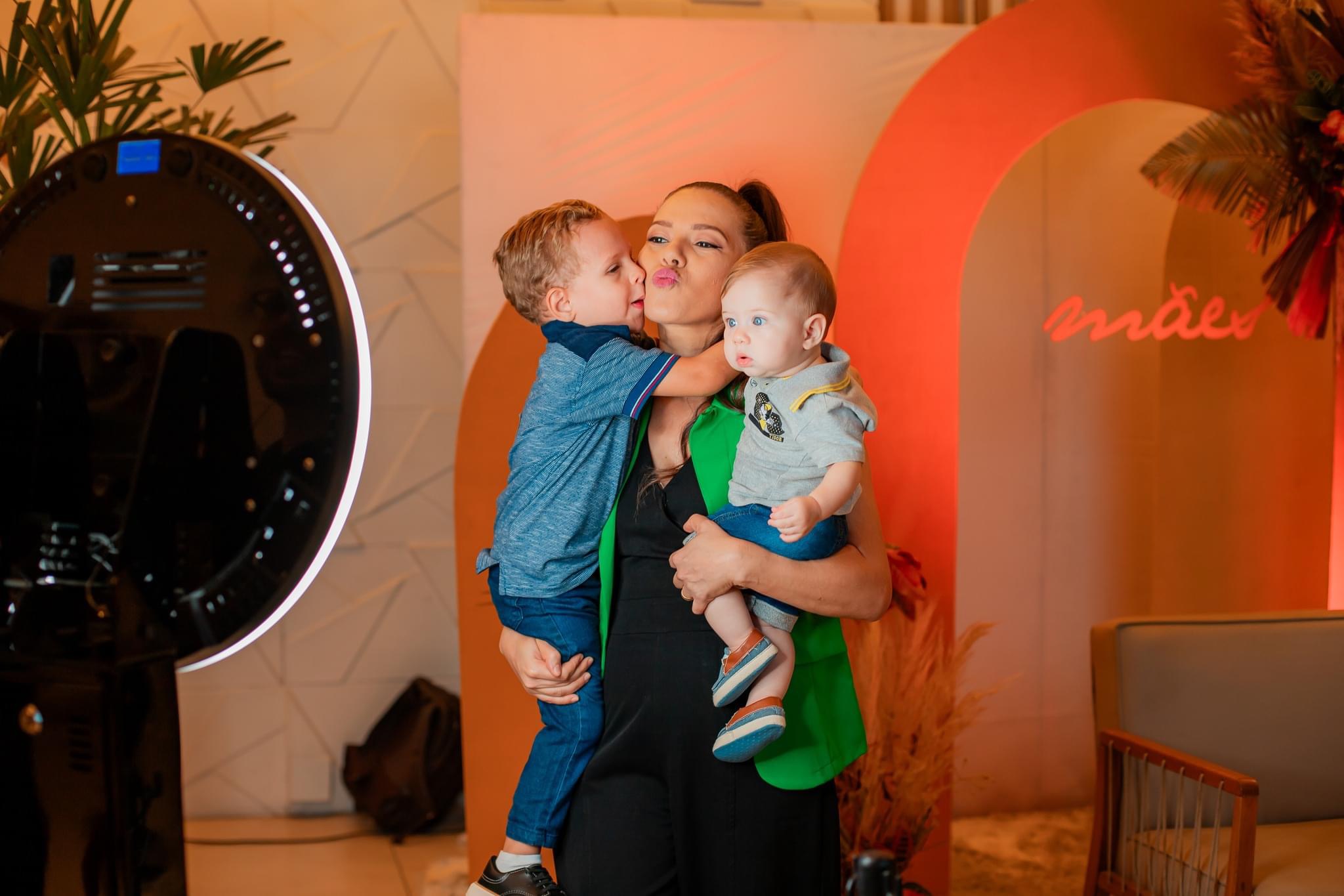 Mãe com dois filhos se divertindo no totem fotográfico em evento Dia das Mães